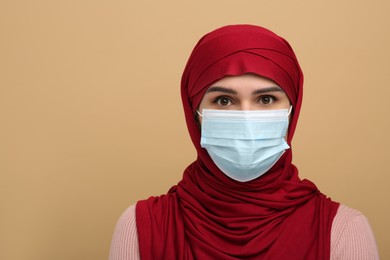 Photo of Muslim woman in hijab and medical mask on beige background, space for text