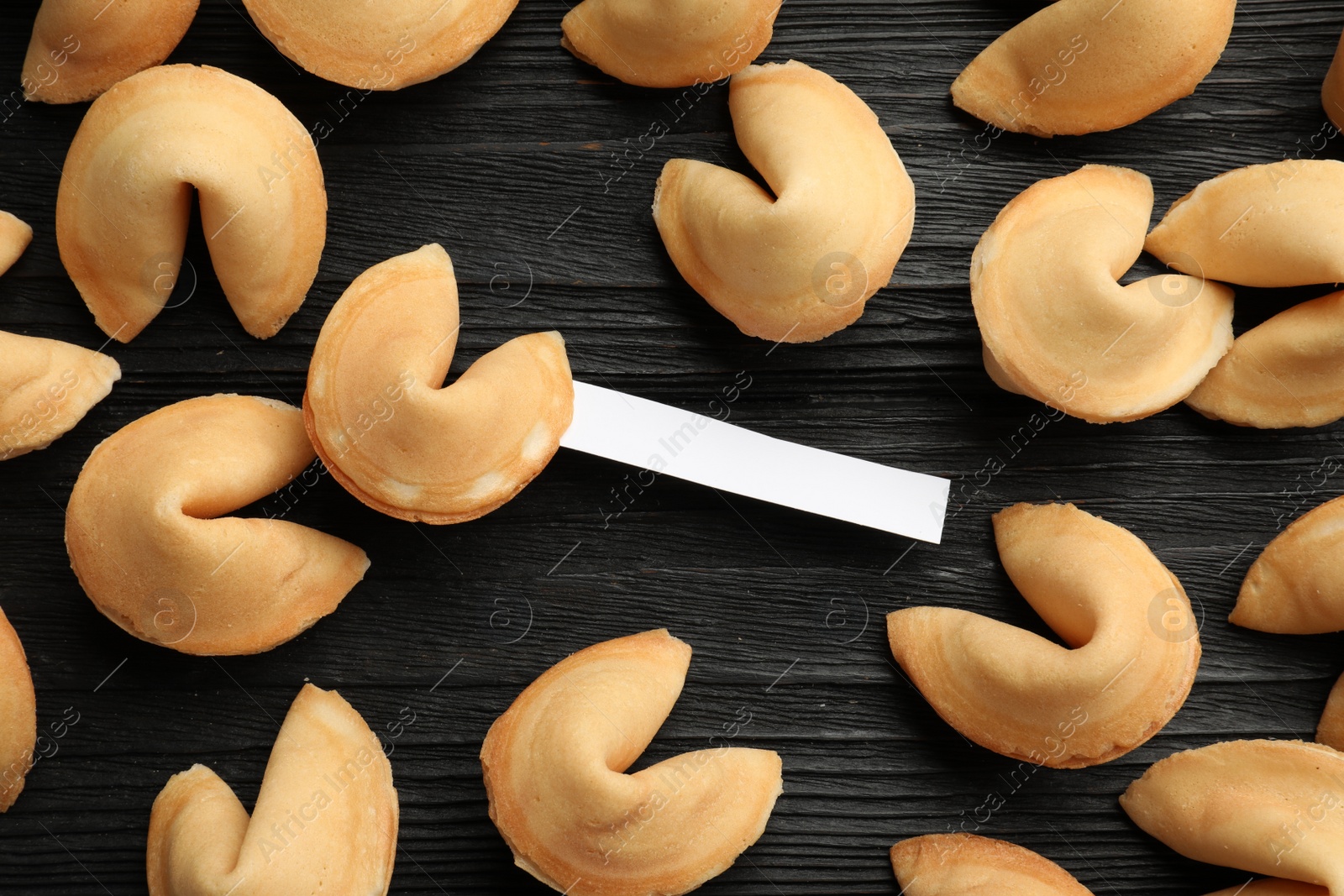 Photo of Tasty fortune cookies with predictions on black wooden table, flat lay. Space for text