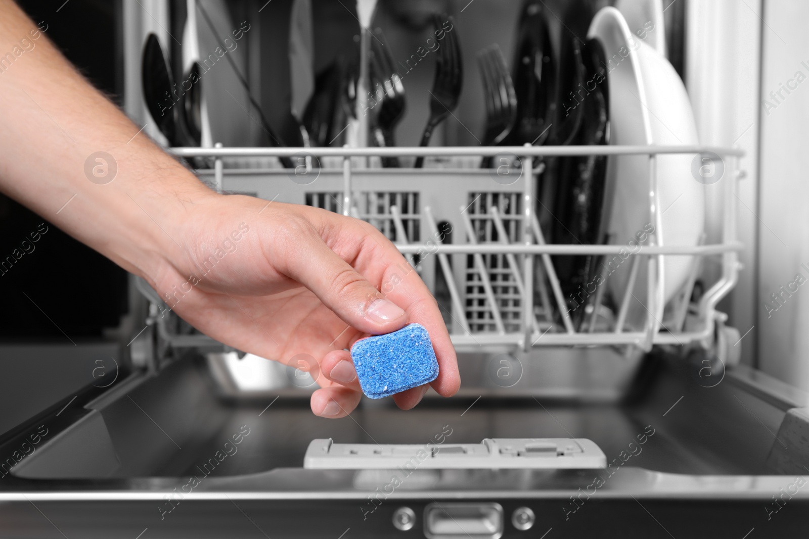 Photo of Woman putting detergent tablet into open dishwasher in kitchen, closeup