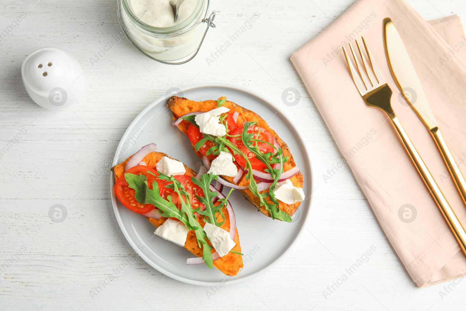 Photo of Plate with stuffed sweet potatoes served on white wooden table, top view