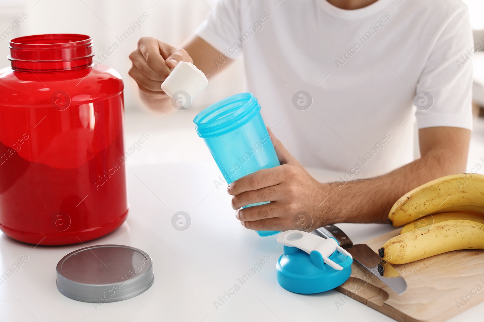 Photo of Young man preparing protein shake at table indoors, closeup