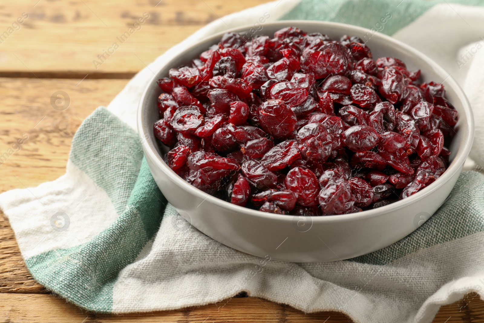 Photo of Tasty dried cranberries in bowl on wooden table, closeup