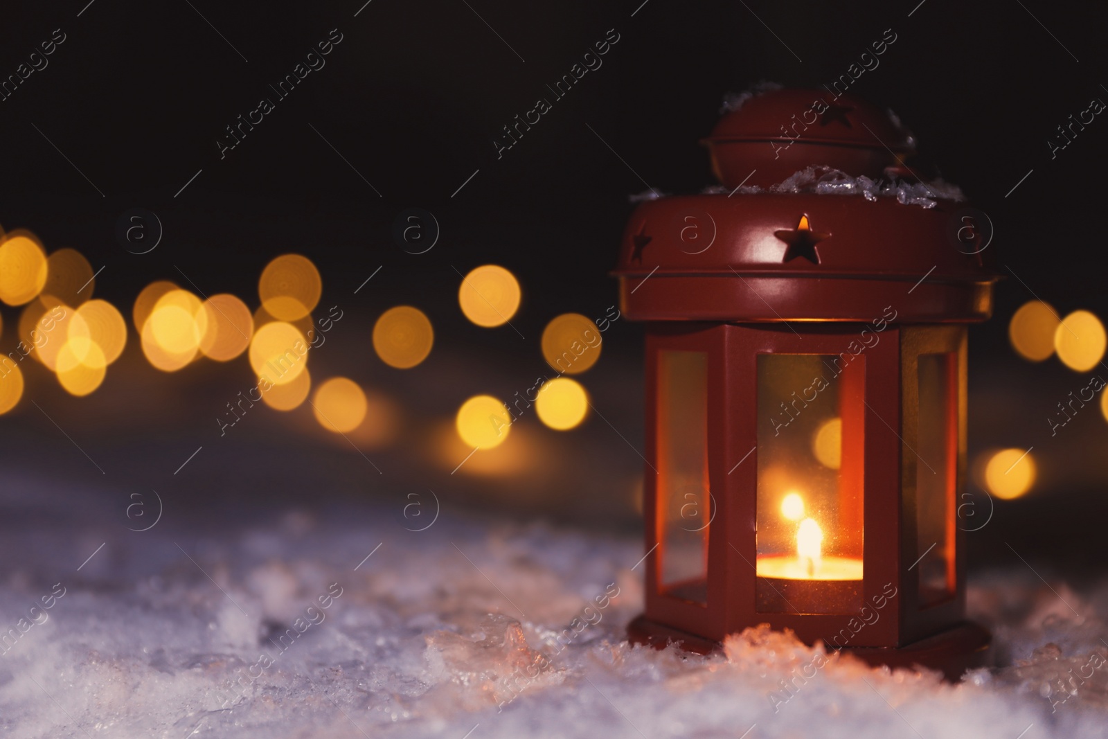 Photo of Lantern with burning candle and Christmas lights on white snow outdoors. Space for text