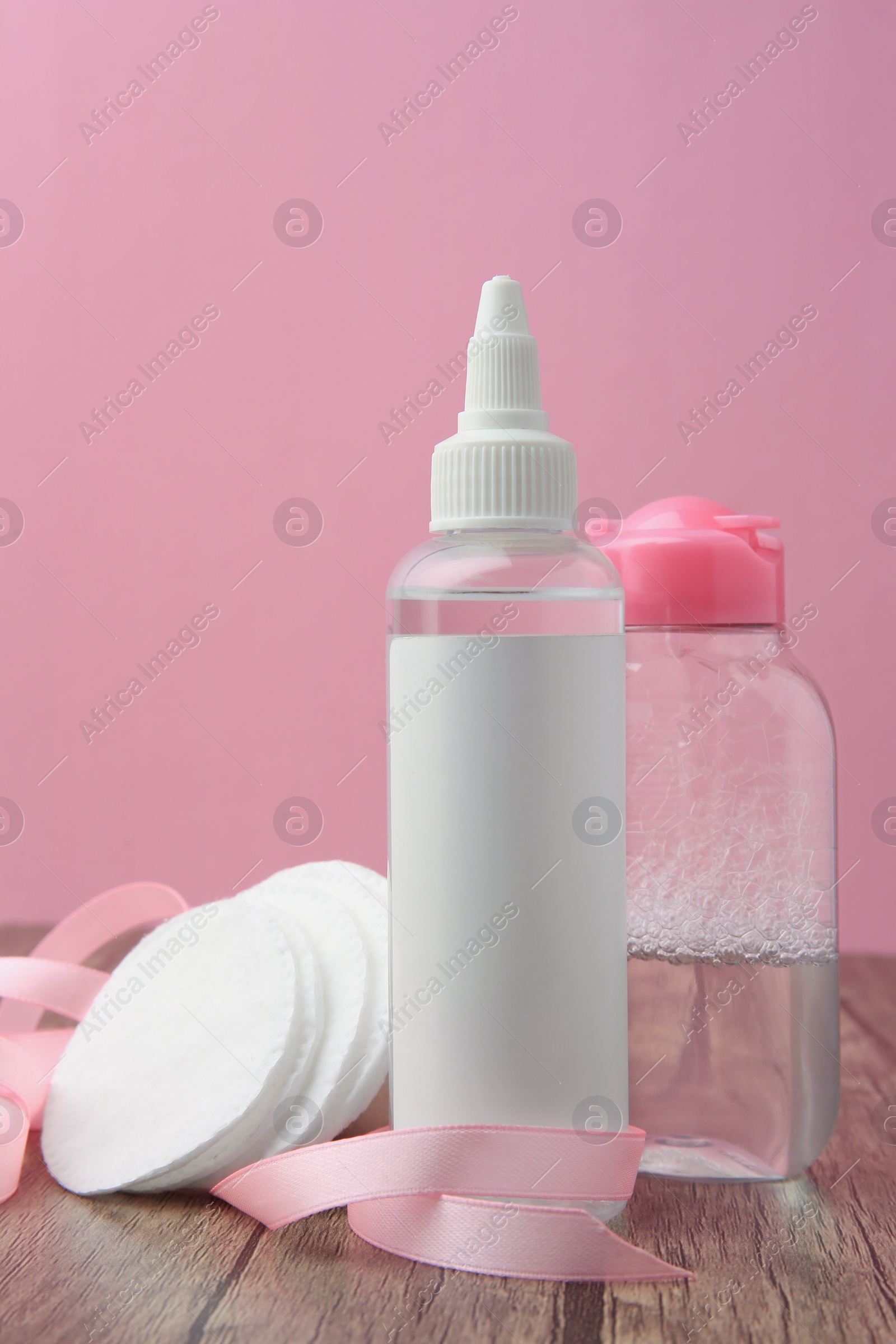 Photo of Composition with makeup removers and cotton pads on wooden table against pink background