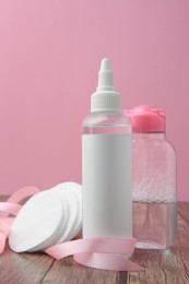 Photo of Composition with makeup removers and cotton pads on wooden table against pink background