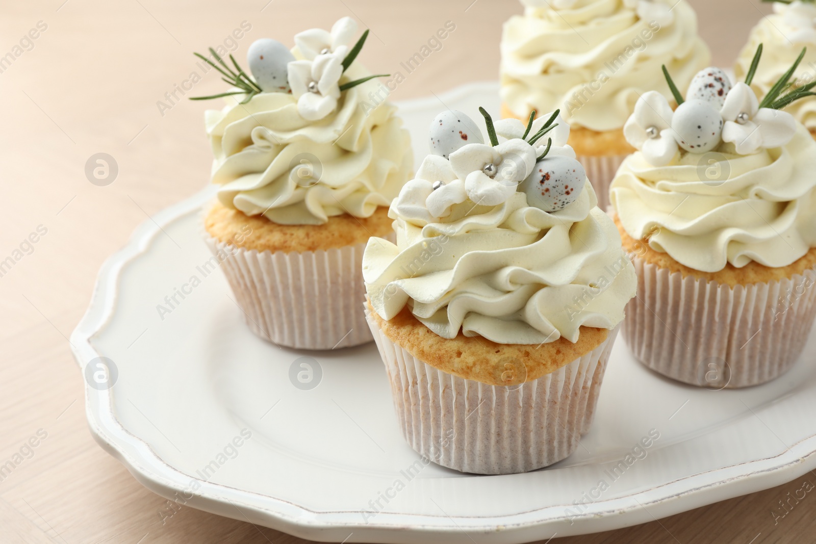 Photo of Tasty Easter cupcakes with vanilla cream on wooden table, closeup