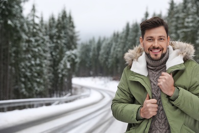 Man in warm clothes near snowy forest, space for text. Winter vacation