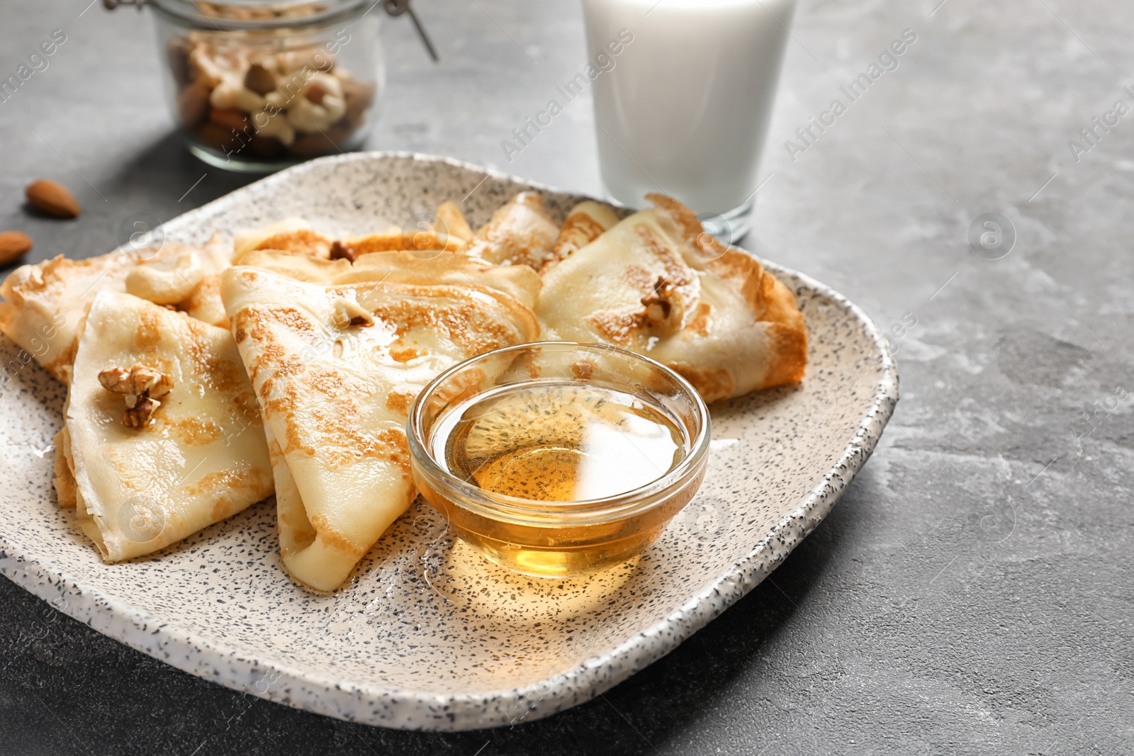 Photo of Thin pancakes served with honey on plate, closeup