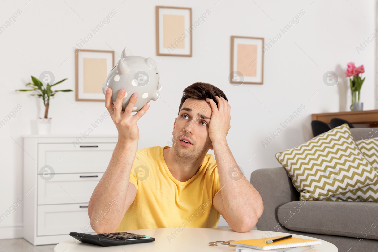 Photo of Sad man looking for money in piggy bank at table indoors