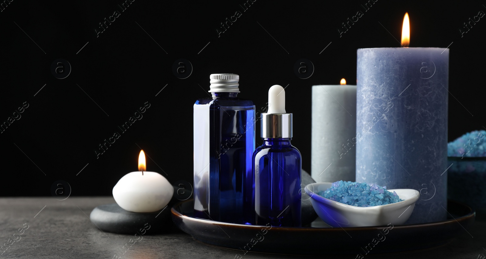 Photo of Spa composition. Cosmetic products, burning candles and sea salt on gray table against black background, space for text