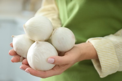 Photo of Woman holding white onions on blurred background, closeup
