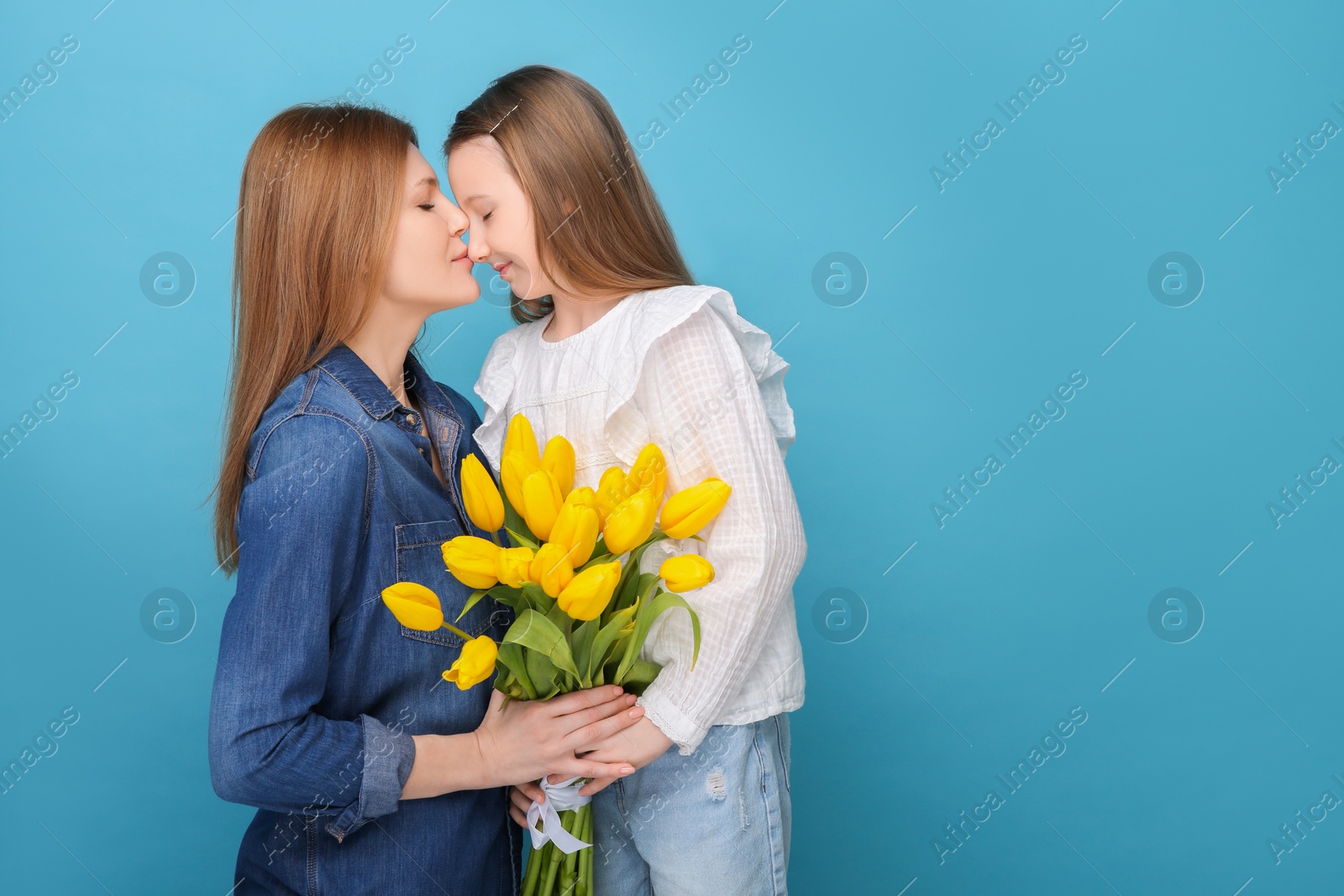 Photo of Mother and her cute daughter with bouquet of yellow tulips on light blue background. Space for text