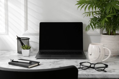 Photo of Office workplace with computer, glasses, cup and stationery on marble table near white wall