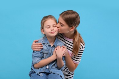 Young woman kissing her little daughter on light blue background. Happy Mother's Day