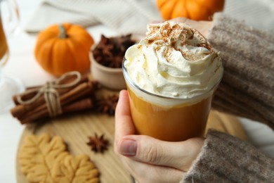 Photo of Woman holding cup of tasty pumpkin spice latte with whipped cream at white table, closeup