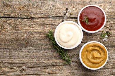 Photo of Different tasty sauces in bowls, rosemary and spices on wooden table, flat lay. Space for text