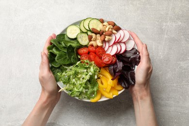 Balanced diet and vegetarian foods. Woman with plate of different delicious products at grey table, top view