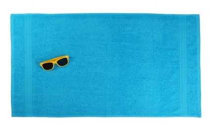 Clean light blue beach towel and sunglasses on white background, top view