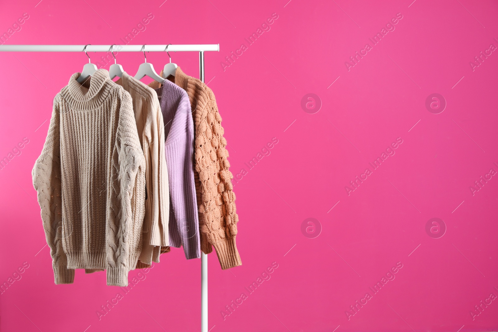 Photo of Collection of warm sweaters hanging on rack against color background. Space for text