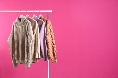 Collection of warm sweaters hanging on rack against color background. Space for text