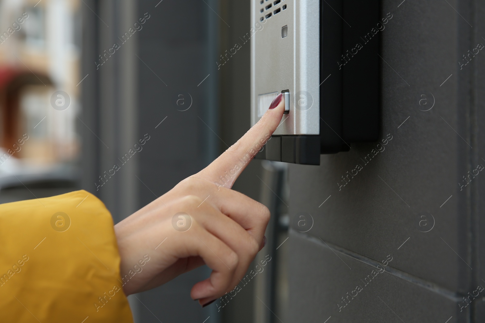 Photo of African-American woman ringing intercom with camera near building entrance, closeup