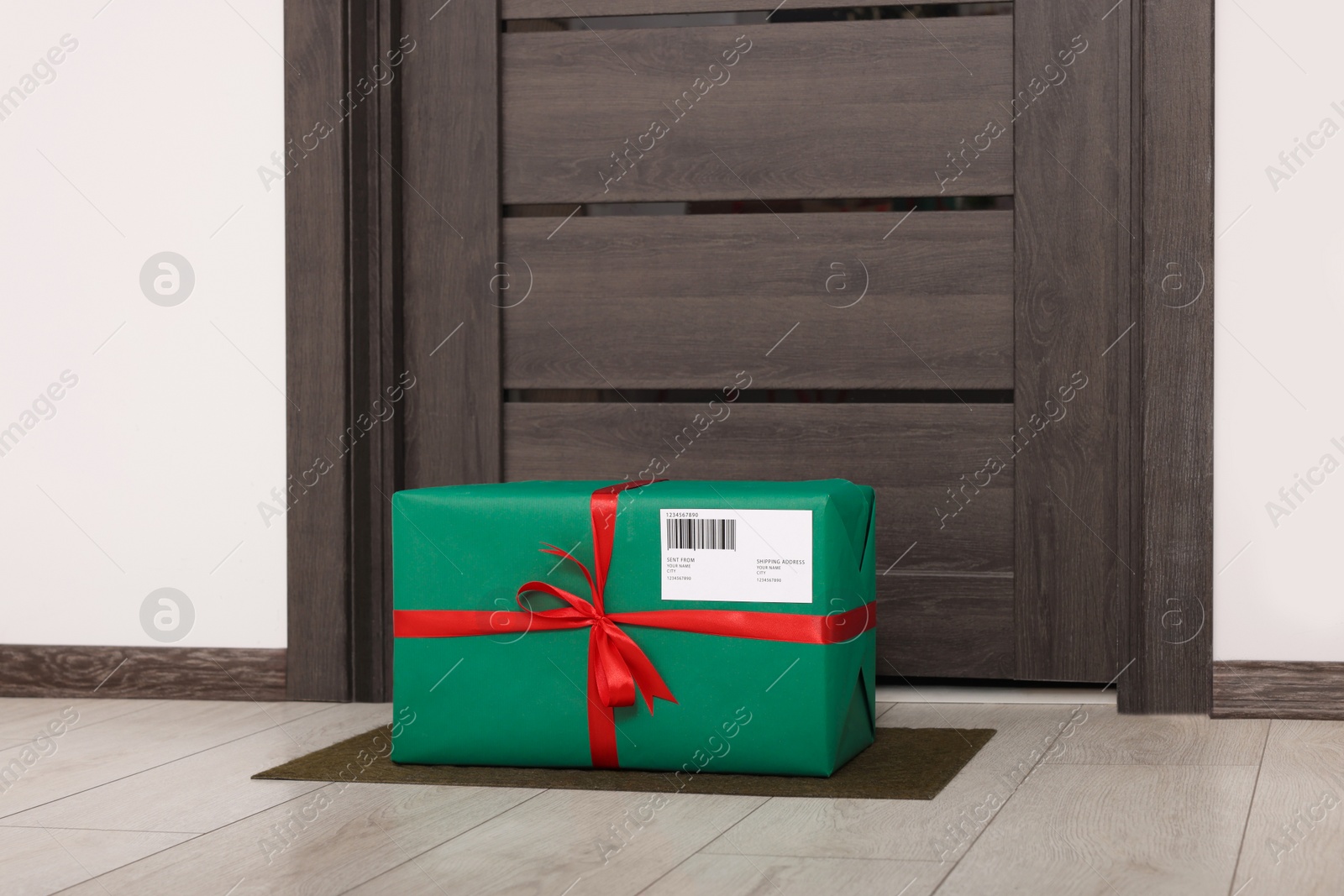 Photo of Christmas gift box on floor near door. Sending present by mail