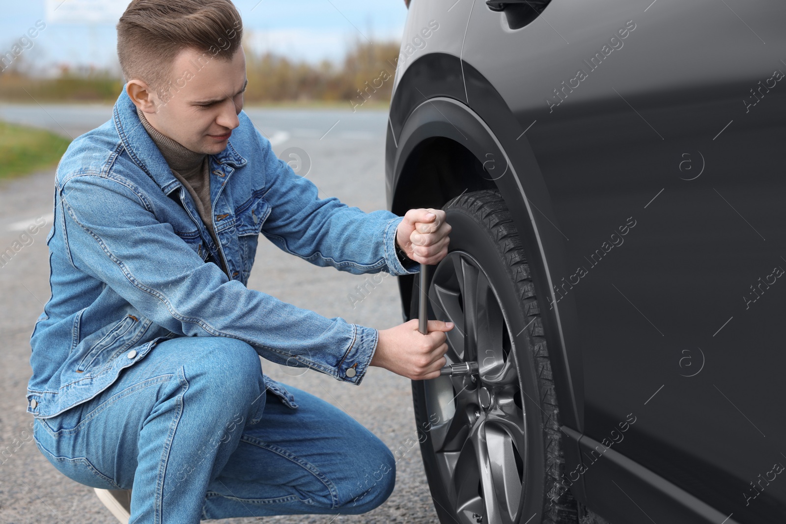 Photo of Young man changing tire of car on roadside