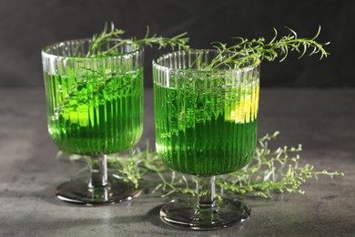 Photo of Glasses of homemade refreshing tarragon drink and sprigs on grey table, closeup