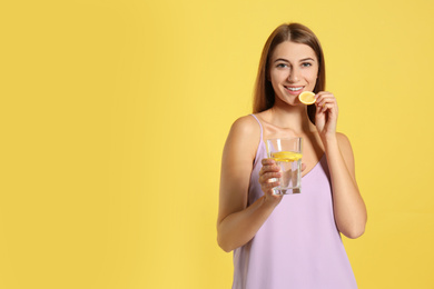 Photo of Young woman with glass of lemon water on yellow background. Space for text