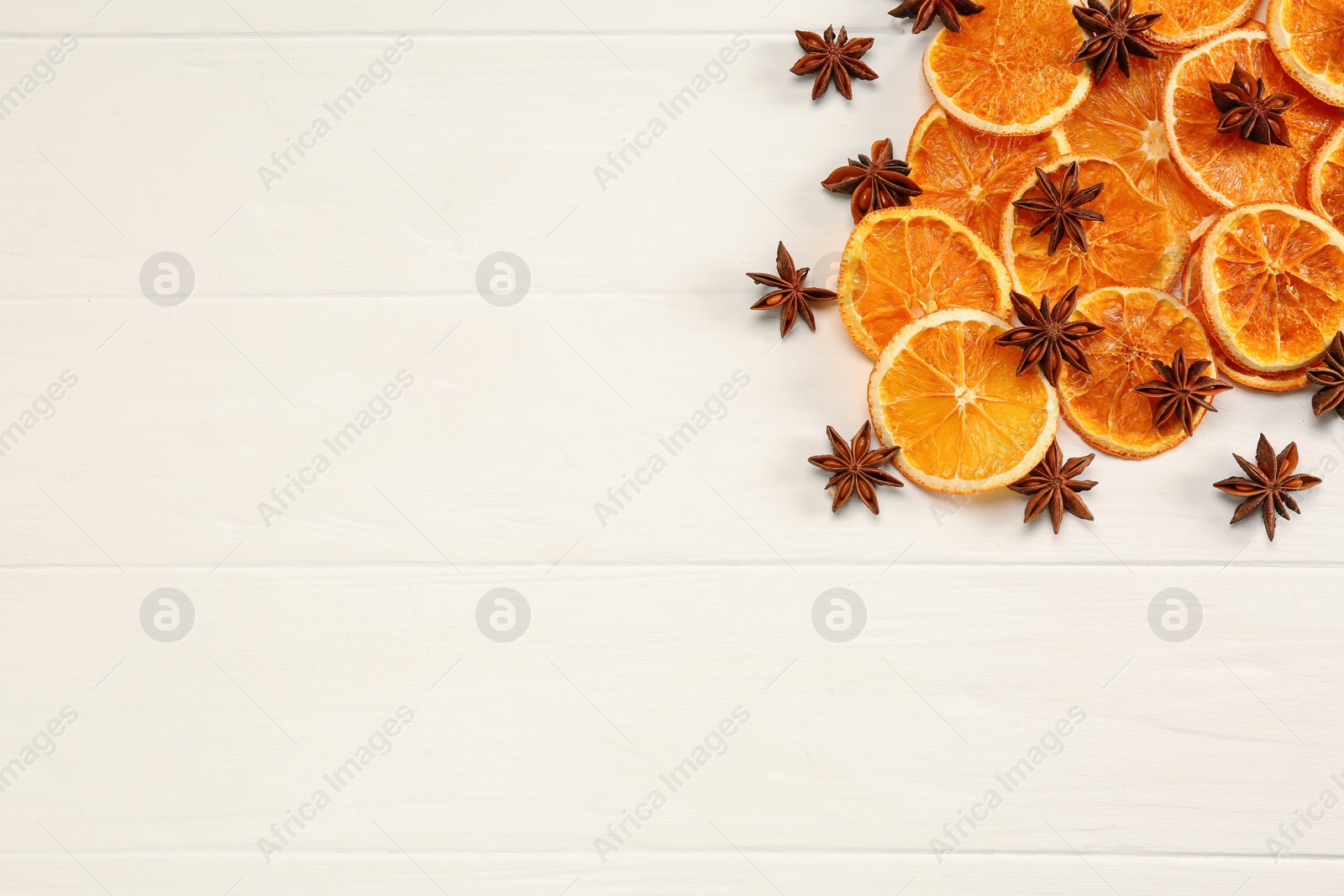 Photo of Dry orange slices and anise stars on white wooden table, flat lay. Space for text