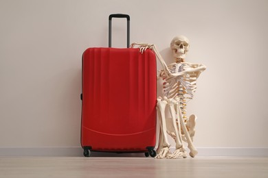 Waiting concept. Human skeleton with suitcase near light grey wall