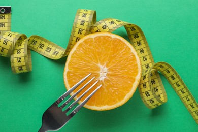 Orange, fork and measuring tape on green background, flat lay. Diet concept