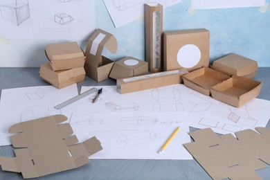 Photo of Creating packaging design. Drawings, boxes and stationery on blue textured table, closeup