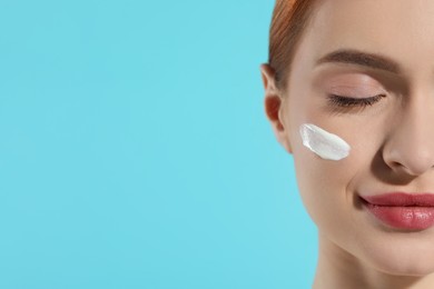 Photo of Beautiful young woman with sun protection cream on her face against light blue background, closeup. Space for text