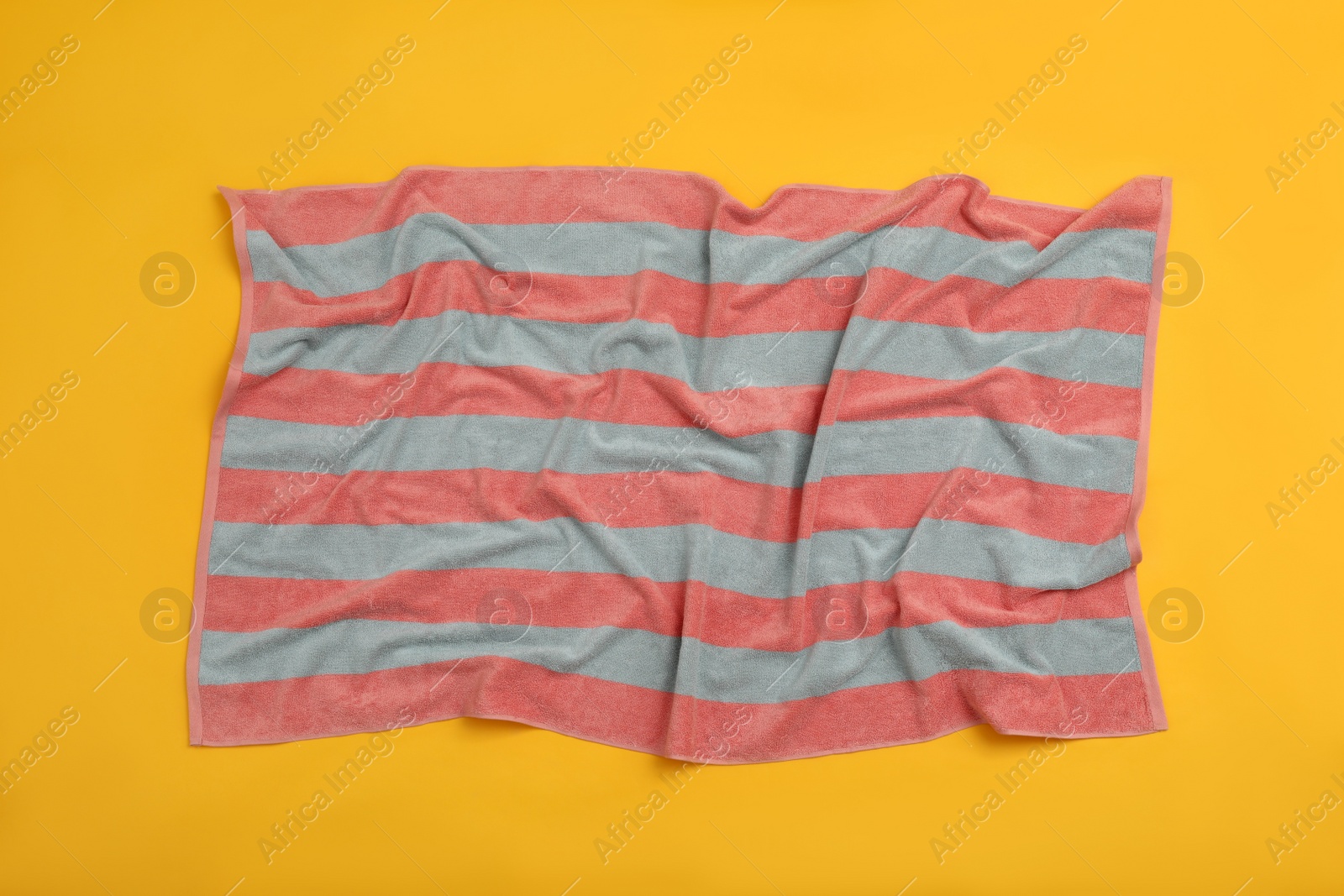 Photo of Crumpled striped beach towel on yellow background, top view