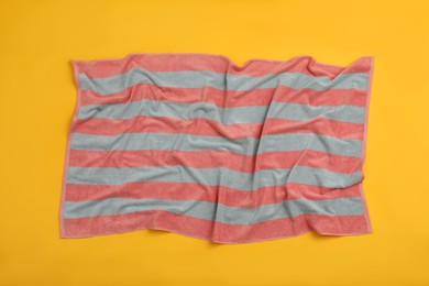 Photo of Crumpled striped beach towel on yellow background, top view