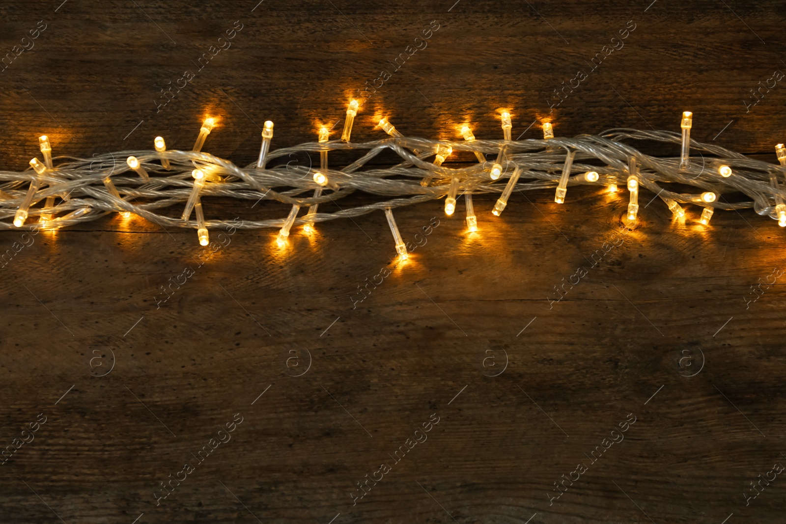 Photo of Glowing Christmas lights on wooden background, top view. Space for text