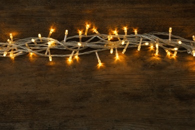 Photo of Glowing Christmas lights on wooden background, top view. Space for text