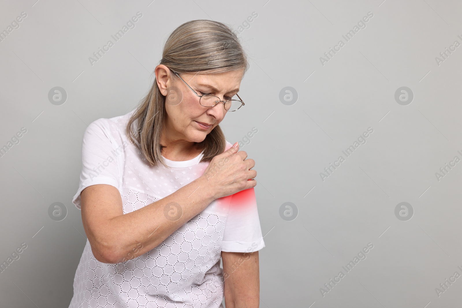 Image of Senior woman suffering from pain in shoulder on grey background. Space for text