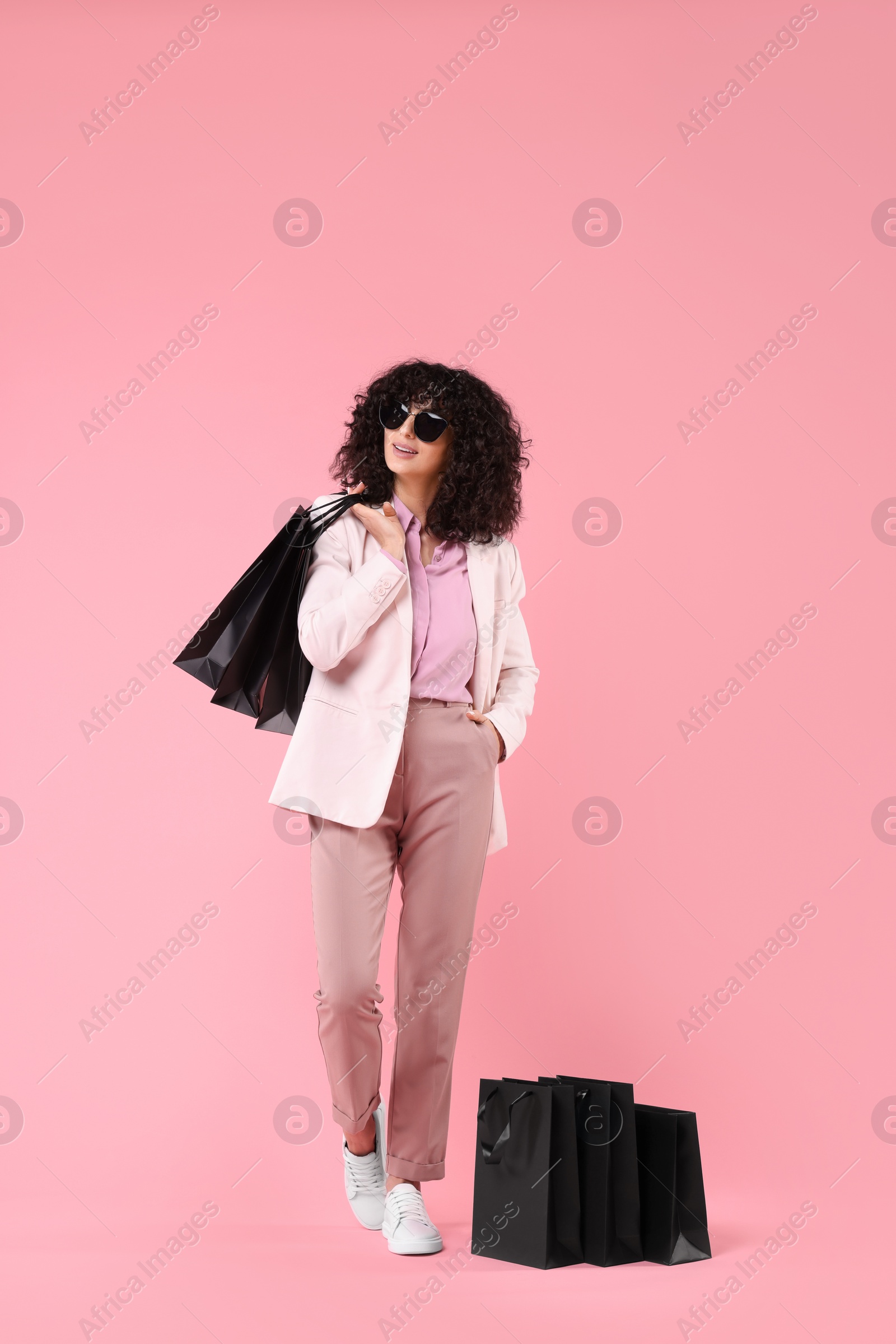 Photo of Happy young woman with shopping bags and stylish sunglasses on pink background