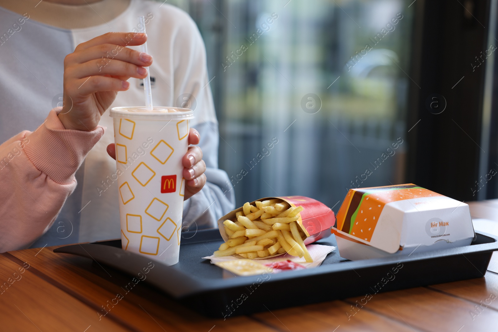 Photo of Lviv, Ukraine - September 26, 2023: Woman with McDonald's drink, burger and french fries at wooden table in restaurant, closeup