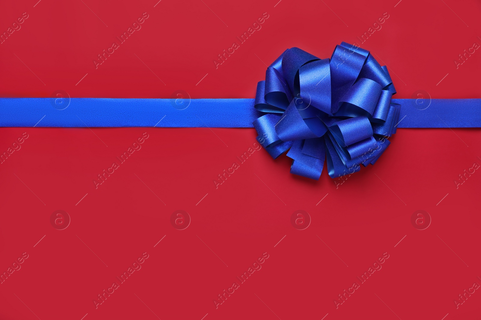 Photo of Blue ribbon with bow on red background, top view. Space for text