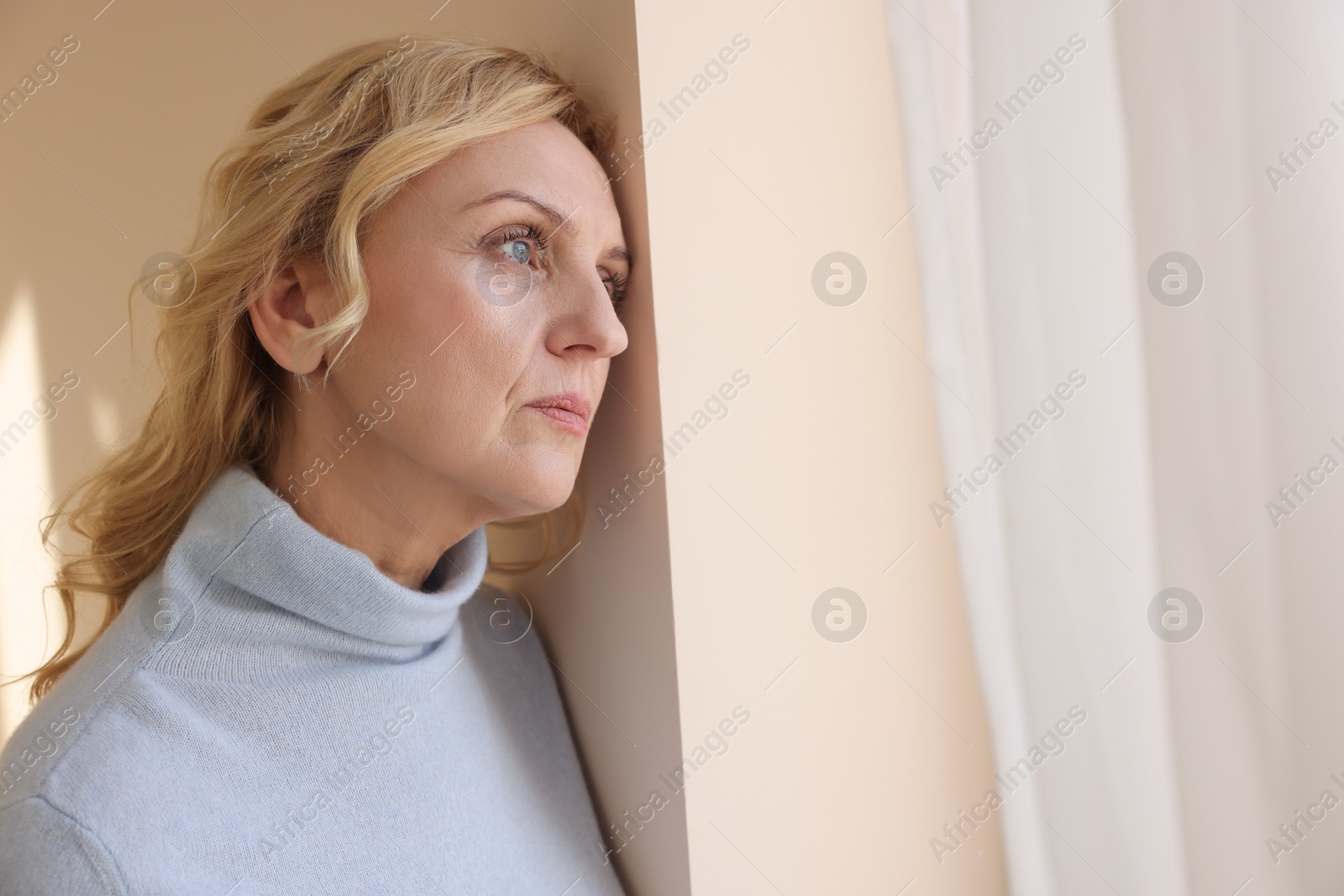 Photo of Upset middle aged woman near window at home. Loneliness concept