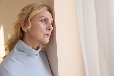 Upset middle aged woman near window at home. Loneliness concept