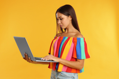 Photo of Beautiful young woman with laptop on yellow background