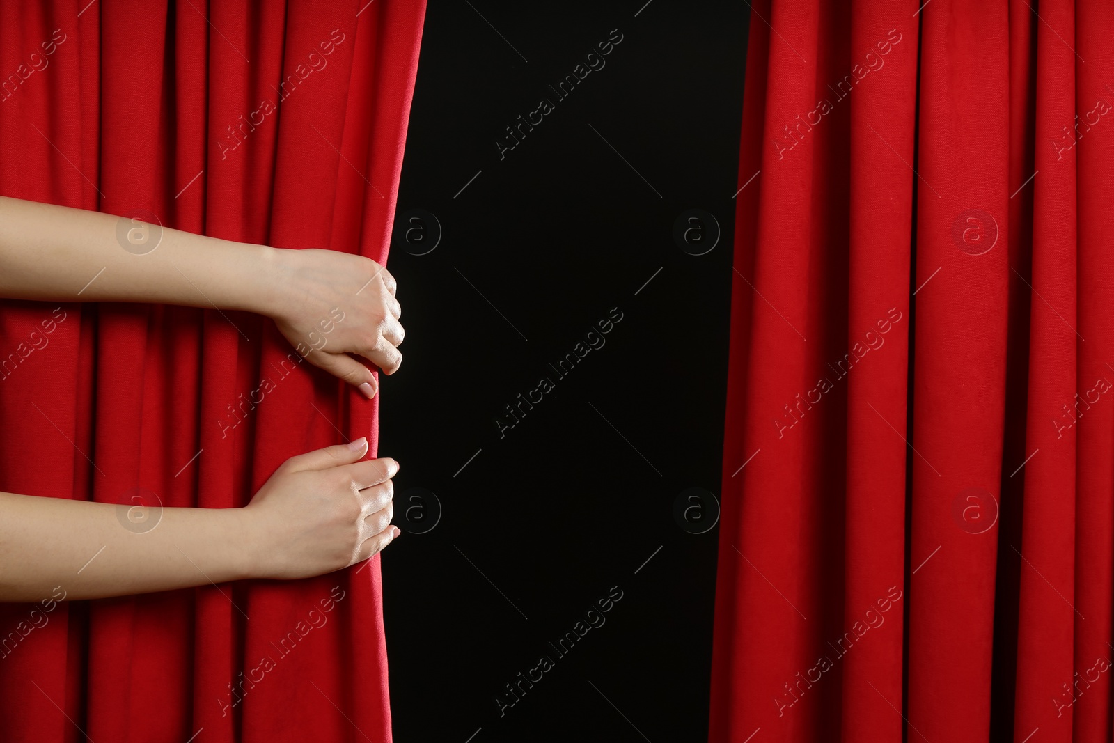 Photo of Woman opening red front curtains on black background, closeup