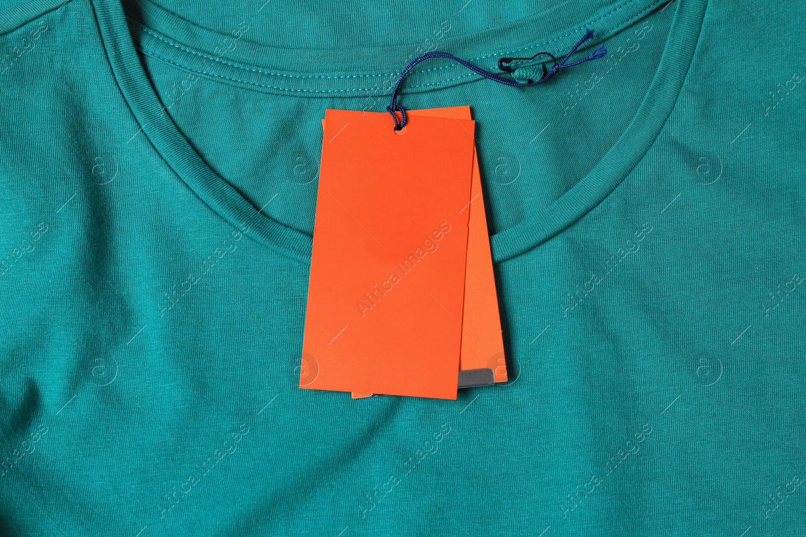 Photo of Blank orange tags on pale green t-shirt, top view. Space for text