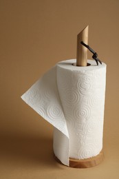 Holder with roll of white paper towels on brown background