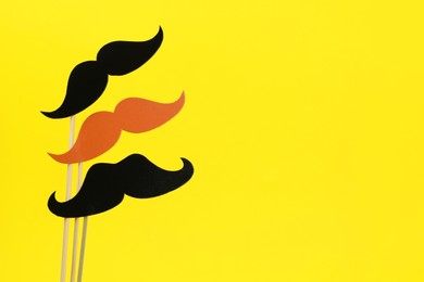 Fake paper mustaches on sticks against yellow background. Space for text
