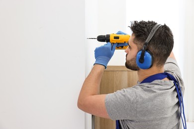 Photo of Young worker in uniform using electric drill indoors. Space for text